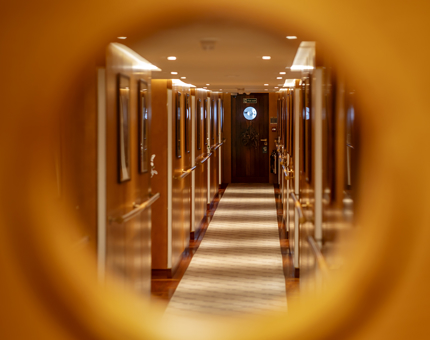 A view of Fingal Hotel's bedroom corridor through the round porthole window of a door. 