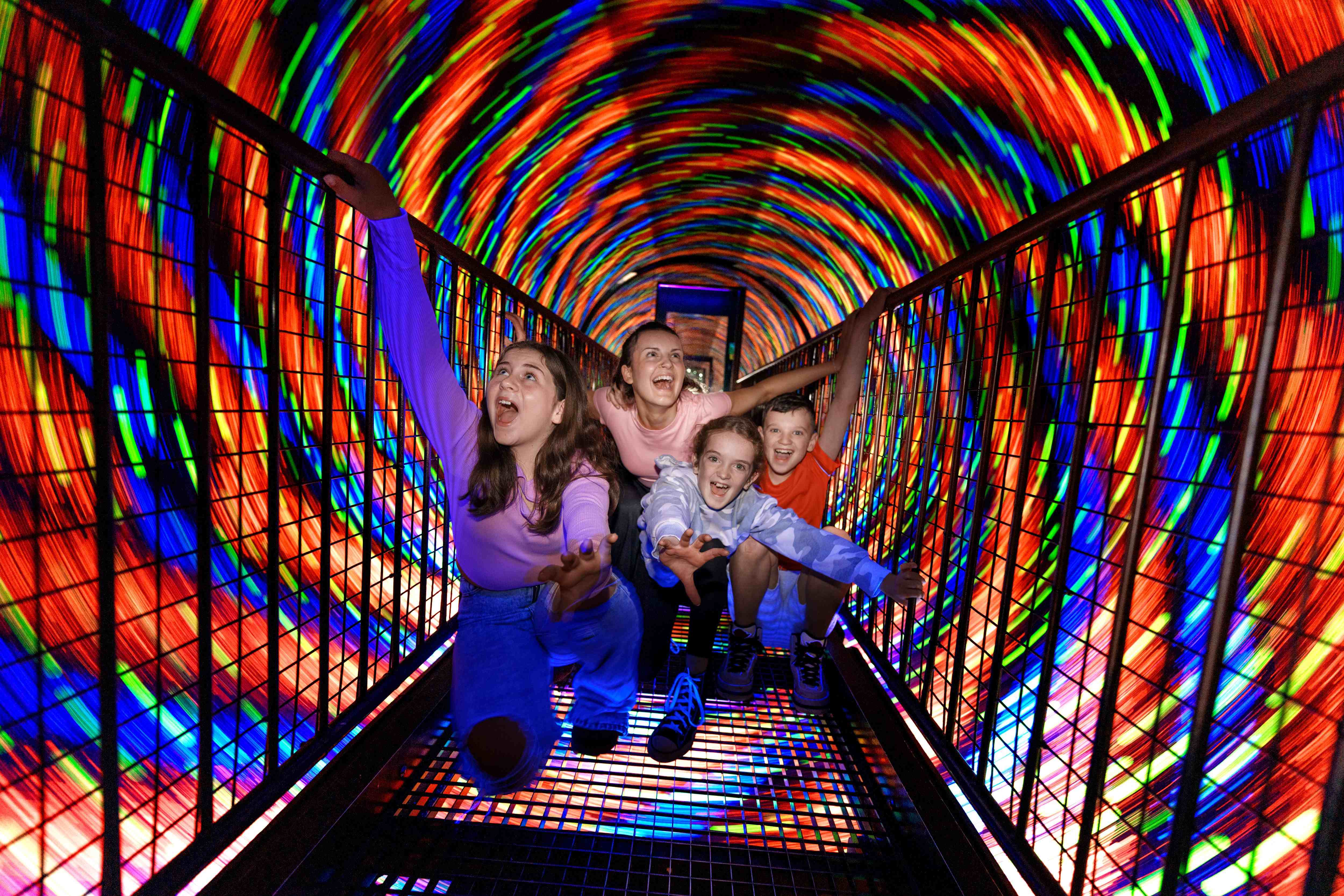 Four people at Camera Obscura indoor activity in Edinburgh. They are on a walkway surrounded by a colourful vortex.