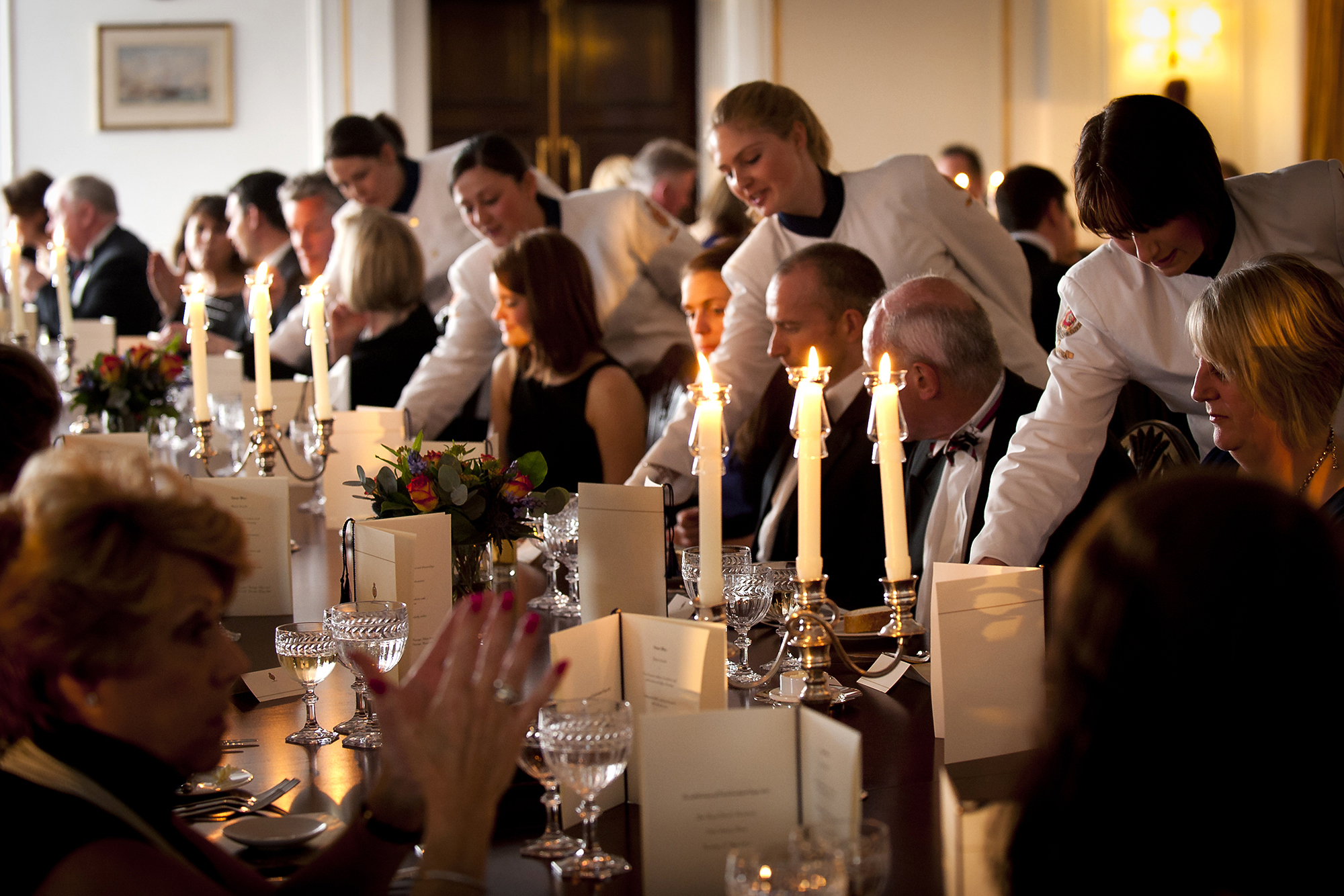 Guests are seated at the table in the State Dining Room being served dinner. 