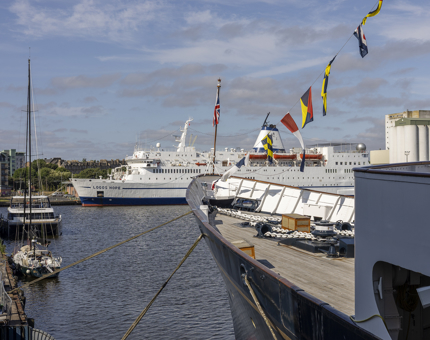 A view from Britannia over the Port of Leith, there is a large white ship and a sail boat. 