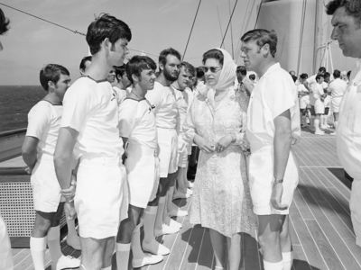 A black and white photo of a woman in a dress speaking to yachtsman on the deck of a ship 