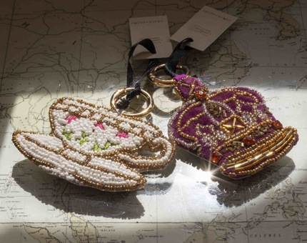 Two beaded hand bag charms. One is a picture of a tea cup and saucer, the other is a crown. 