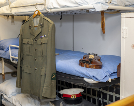 In the Royal Marines' Barracks a uniform is hanging from the bunks. A violin and cap are placed on the bunks.