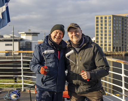 Two Maintenance men standing on the decks of Fingal Hotel in Leith holding paint rollers. 
