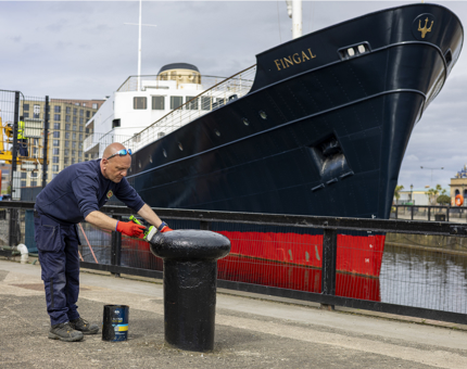 A man painting a bollard with black paint on the quayside at Fingal Hotel. 