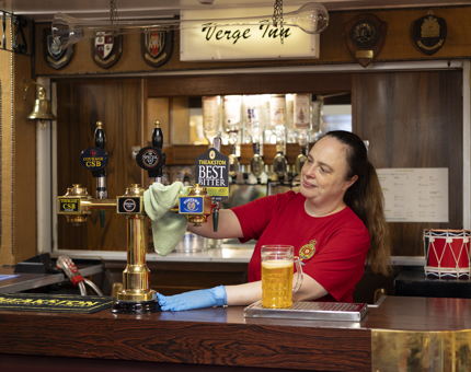 A Housekeeper is in the POs mess behind the bar cleaning brass work on beer taps. 