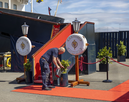 A Facilities Officer is watering plants next to Britannia's Royal Brow in Edinburgh. There is a red carpet on the ground leading up to it.