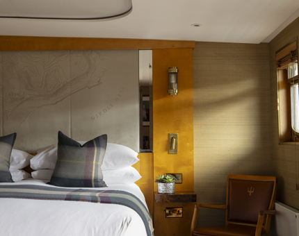 A cabin aboard Fingal Hotel. There is a map on the headboard, and tartan pillows. 