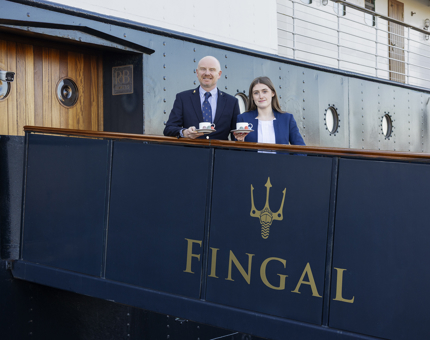 Two people standing on the gangway to Fingal Hotel's entrance holding coffee cups. 