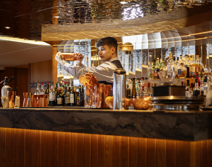 A barman is shaking a cocktail behind the bar in the Lighthouse Restaurant aboard Fingal in Leith. 