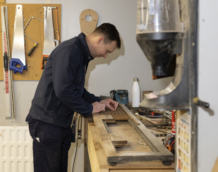 A Maintenance team member is at a work bench adding lattice details to a scupper board. 