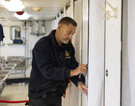 A Maintenance man fixing a hook to the wall in an onboard bathroom. 