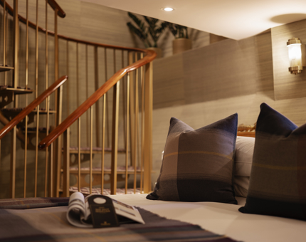 A close look at a bed with square pillows with tartan pillowcases. There is a spiral staircase in the background. 