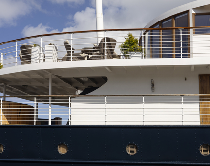 A side view of a section of Fingal Hotel. There is a sun deck at the top with tables and chairs on it. 