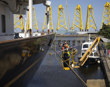 Two maintenance men are on a yellow cherry picker, washing the side of Britannia in the Port of Leith. 