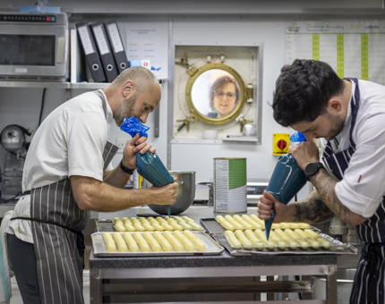 A visitor looks on as Executive Pastry Chef, Stephen, and Junior Sous Chef, Bob, prepare petits fours