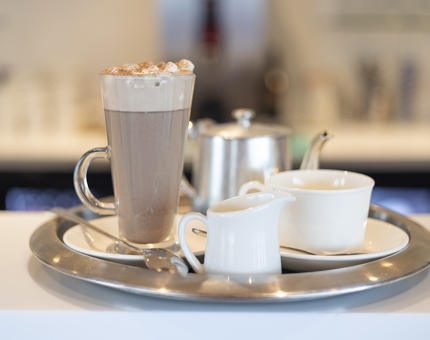 A silver tray with a hot chocolate with cream and marshmallows, a milk jug, cup and small silver teapot.
