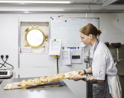 A Chef is Taking Freshly Made Bread Rolls Out The Oven In The Galley on board Britannia. 