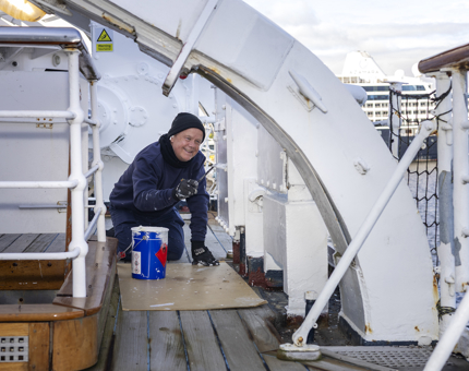 A Maintenance team member is keeling on deck to add a coat of paint to a hard to reach spot!
