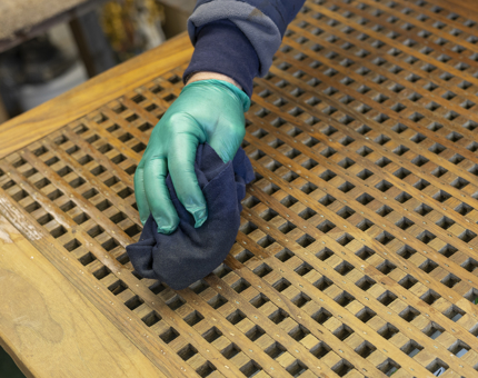 A close up of a hand wearing a green glove oiling a wooden lattice.