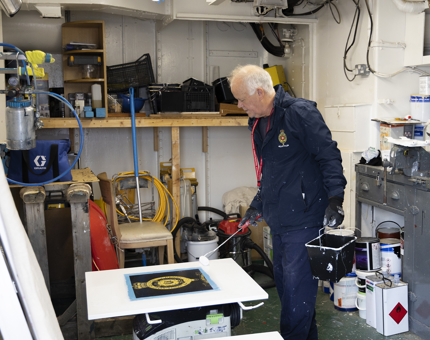 A stair gate with the crest of Britannia is getting a new coat of paint by a maintenance man. 