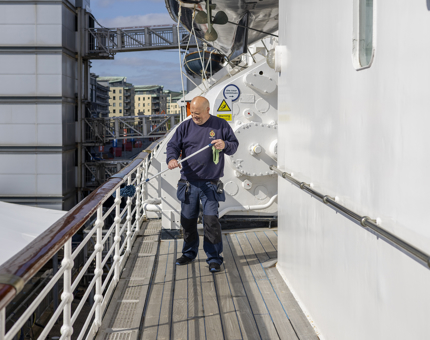 A member of the Facilities team polishing handrails on an outside deck on the tour route. 