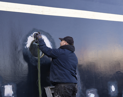 A maintenance team member sanding the hull of Britannia in the Port of Leith. 