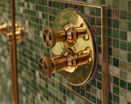 Brass Nautical Tap Details found in a cabin's Bathroom. The tiles in the background are green. 