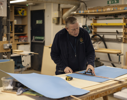 In the workshop, a maintenance man is cutting non-slip tread for the Royal Barge. 