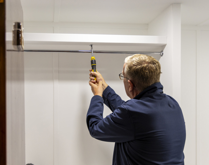 A maintenance man attaching a hanging railing into a cupboard. 