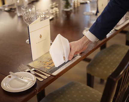 A close up of a hand placing a folded napkin on a placemat in the State Dining Room. 