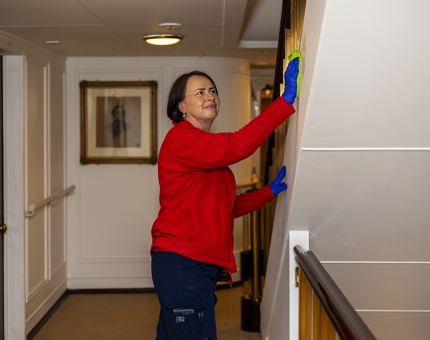 A Housekeeper wearing a red fleece jacket is wiping the side of a staircase. 