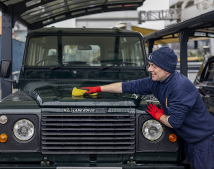 A man is using a yellow cloth to polish a dark green Land Rover on Britannia's quayside in Leith. 
