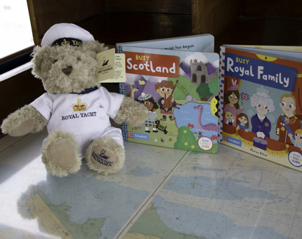 A Britannia novelty teddy bear sits next to two children's picture books - one about Scotland and the other about The Royal Family.