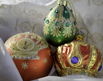Three brightly coloured Christmas bauble decorations nestled in tissue paper. One red, one green and one shaped like a crown.