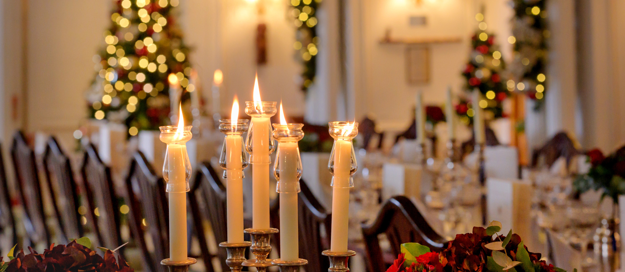 A long table is set with lit candles for a formal dinner, with soft fairy lights on decorations in the background