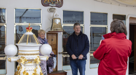 Two visitors posing for a photograph on the Verandah Deck as a Visitor Assistant takes their picture. 