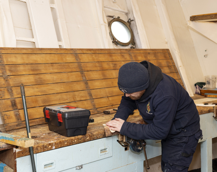 A man is sanding a handrail from Britannia's activity boat. 