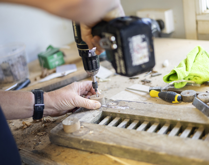 A close up of a person holding a power drill as they refurbish a scupper board. 