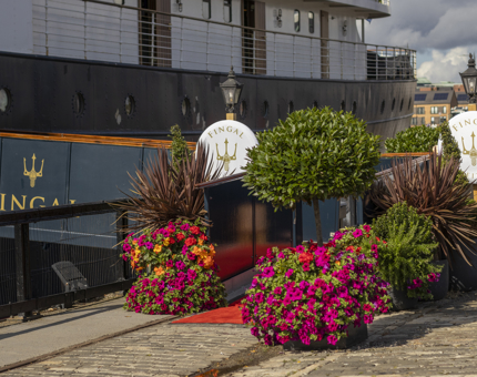 The entrance to Fingal hotel in the Port of Leith. There are plants and flowers adorning the entrance of the walkway up to the ship. 