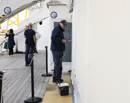 A maintenance man is painting the Starboard side of Britannia white. 