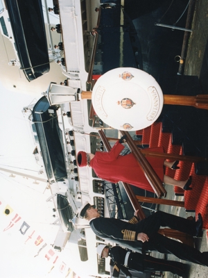 A woman in a red suit and a man in a black suit walking up a brow of a ship