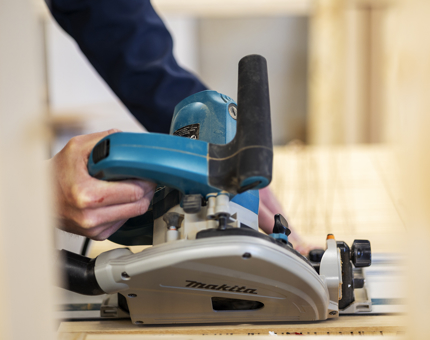 A Maintenance team member using a circular saw to make a desk. 