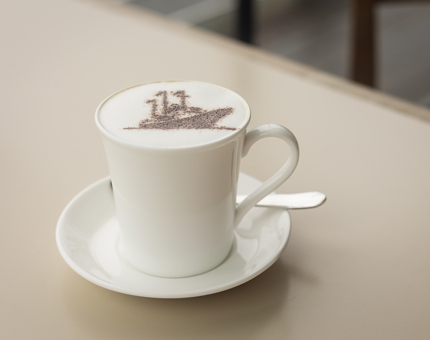 A cappuccino with a chocolate stencil of a ship on top of it. 