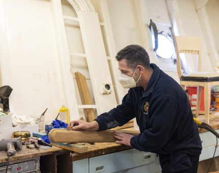 A maintenance team member preparing a handrail prior to varnishing. 