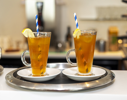 Two glasses of iced tea. They have blue and white straws in the glasses and garnished with a slice of lemon. 