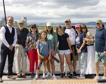 Visitors posing for a photo together on Britannia's Bridge in Edinburgh. In the background there is a view of the Port of Leith. 