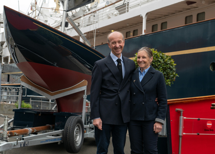 A man and woman standing next to Royal Racing Yacht Bluebottle at The Royal Yacht Britannia in Leith. 