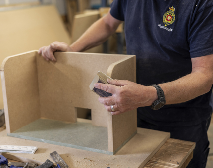 A close up of a maintenance man sanding a wooden shelf. 