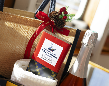 A close up of a bar of Britannia chocolate and bottle of fizz with a calico bag behind it. 